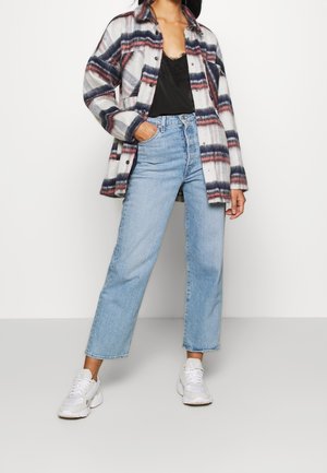 Camisa de franela de cuadros de gran tamaño en gris, rojo y azul marino, llevada sobre una blusa de encaje negra. Combinada con jeans rectos de color azul claro y zapatillas blancas.