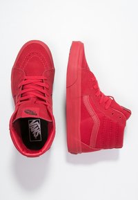 Zapatillas altas rojas hechas de ante y lona, con cordones en tono, un cuello acolchado y una suela de goma texturizada con detalles de costura.