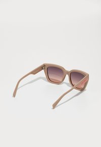 Beige sunglasses with a cat-eye shape, gradient tinted lenses, and logo accent on the temple. Made from a smooth plastic material.
