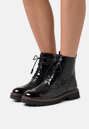 Black patent leather ankle boots with a textured finish, lace-up design, and thick rubber sole. Features decorative stitching and side zipper.