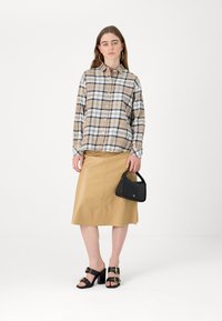 Plaid button-up shirt in beige and navy, paired with a tan leather skirt. Black heeled sandals, gold buckles, and a black handbag.