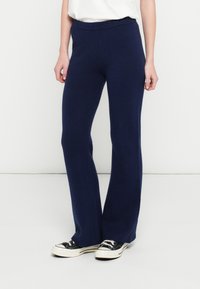 Navy blue flared pants made from a soft knit material with a ribbed waistband, paired with black and white sneakers.