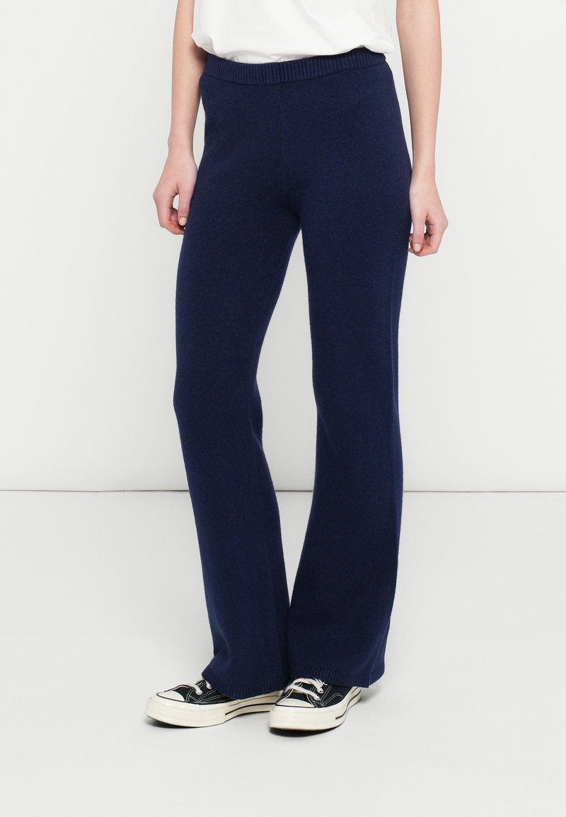 Navy blue flared pants made from a soft knit material with a ribbed waistband, paired with black and white sneakers.