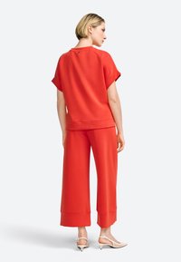 Červený dvoudílný outfit skládající se z krátkého topu s krátkým rukávem a kalhot s širokými nohavicemi, vyrobený z hladkého materiálu a s volným střihem.