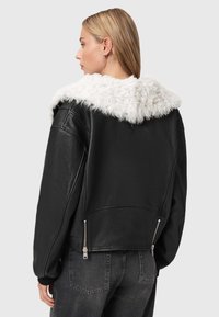 Sort læderjakke med en hvid faux fur-krave, har en afslappet pasform, lynlåslommer i siden og ribbede manchetter. Glat tekstur.
