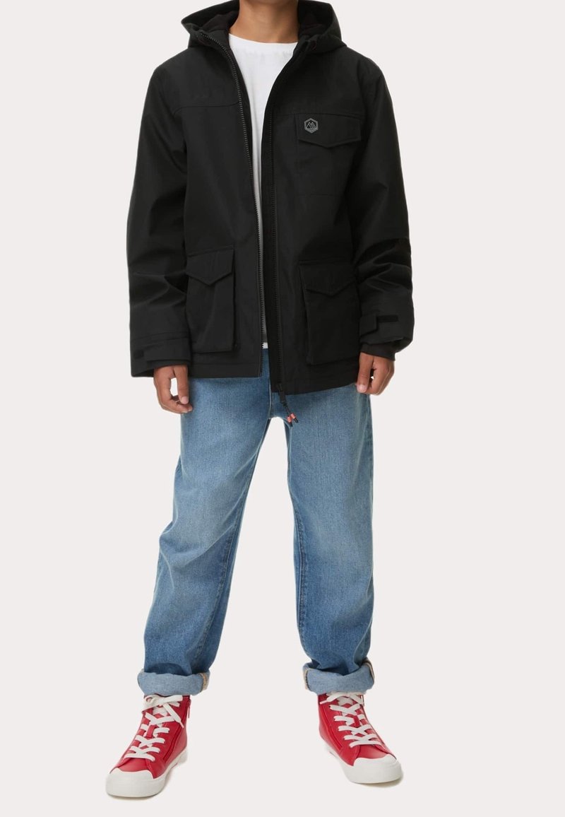 Personne portant une veste à capuche noire, un jean bleu clair avec revers, une chemise blanche et des baskets montantes rouges avec des lacets blancs.