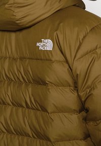 Brown puffer jacket with a hood, featuring quilted sections and the white embroidered logo of The North Face on the left shoulder.