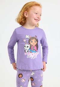 Lange mouwen paars shirt met een illustratie van een meisje en een kat met bloemmotieven; gecombineerd met paarse legging met tekenfilmgezichten en bloemen.