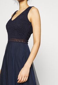 Abito blu navy con corpino in pizzo dall scollatura a V e design senza maniche, abbinato a una gonna fluente realizzata in tessuto leggero.