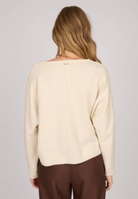 Pull crème avec une coupe carrée, des poignets côtelés et un détail de couture verticale au dos, fabriqué en tissu doux et texturé.
