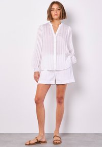 Weißes Hemd mit Knopfleiste, vertikalen Streifen, langen Puffärmeln und passenden Shorts. Leichter Stoff, entspannte Passform, schlichtes Design.