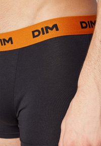 Svarte boksershorts med oransje midjebånd som har svart "DIM"-logo. Stoffet ser glatt ut med en tettsittende passform.