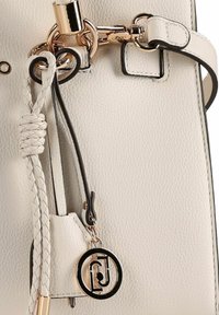 Witte leren handtas met een korrelig oppervlak, gouden accenten, een gevlochten banddetail en een cirkelvormige logohanger.