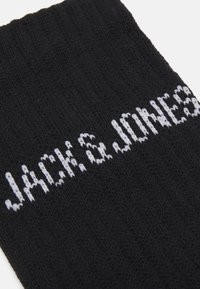 Calzino nero lavorato a maglia con testo bianco "JACK & JONES". Il tessuto ha una texture morbida e un design a coste lungo il polsino.