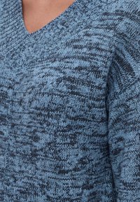 Gros plan d'un pull tricoté bleu et noir avec un col en V côtelé porté par une personne.