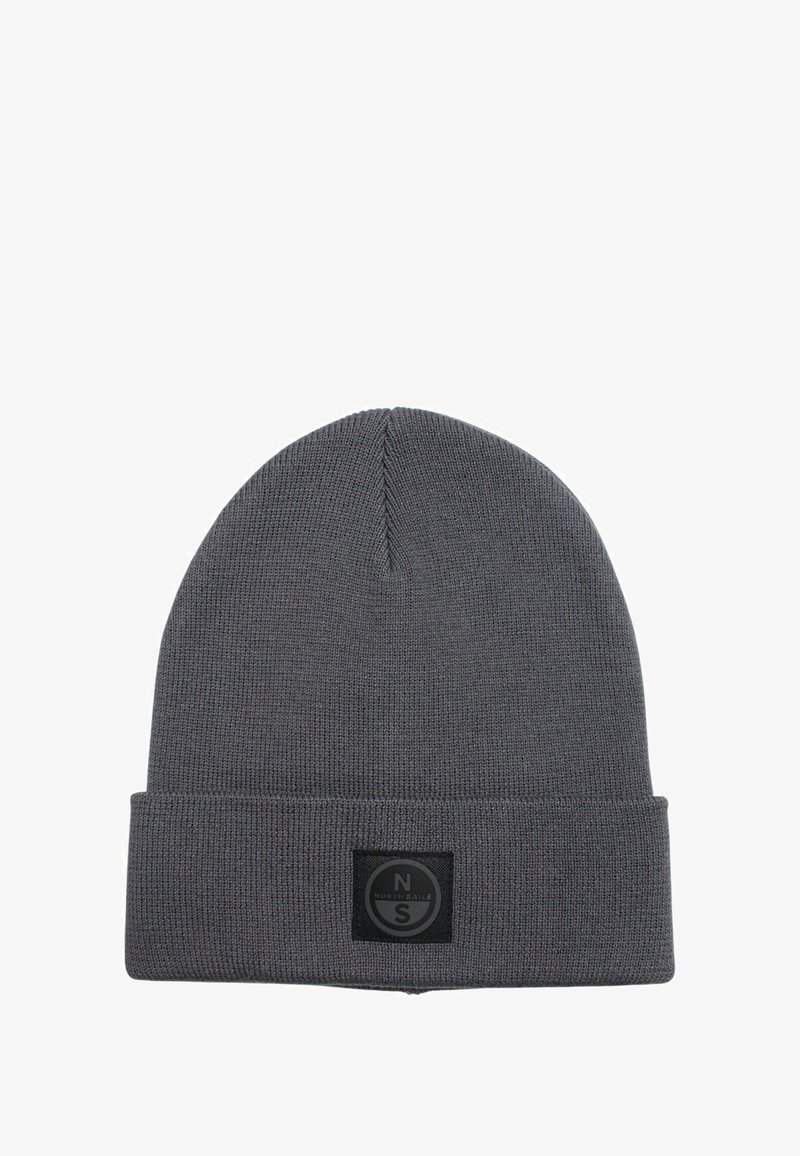 Gorro de punto gris con puño doblado, que presenta un parche de logo circular negro en la parte frontal. Textura suave y ajuste ceñido.
