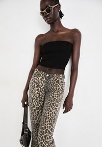 Top noir sans bretelles associé à un jean imprimé léopard avec taille haute, coupe ajustée et une poche arrière. Les accessoires comprennent des lunettes de soleil étroites.