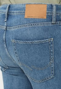 Μπλε τζιν παντελόνι από τζιν ύφασμα με δερμάτινο ταμπελάκι στη πίσω ζώνη μέσης και πίσω τσέπη με διακοσμητική ραφή.