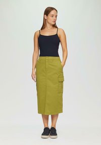 Olijfgroene cargoskirt met een rechte snit, tot op de knie, met twee zijzakken, gecombineerd met een zwart tanktop en zwarte sneakers.