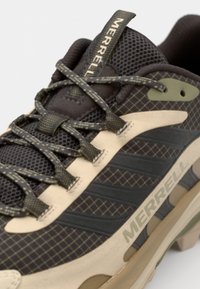 Merrell hiking shoe featuring a dark brown mesh upper with grid pattern, beige rubber midsole, olive green accents, and textured laces.
