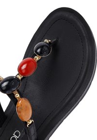 Sandalo nero con suola piatta, caratterizzato da una striscia di gioielli decorata con pietre nere, rosse e ambra incastonate in una struttura dorata.