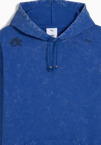 Blå bomullshoodie med en texturerad finish, med svarta logotyper på bröstet. Snörhuva och känguruficka ingår.