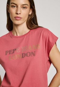 Rausvos medvilnės marškinėliai su apvaliu iškirpimu ir trumpomis rankovėmis, papuošti tekstu "PEPE JEANS LONDON" žibančiais akmenukais.