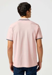 Jasnoróżowa koszulka polo z krótkim rękawem i granatowym kołnierzykiem. Miękka tkanina, prosta krawędź i boczne rozcięcia dla wygody.