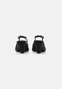 Tacchi slingback in suede nero con una forma strutturata, dotati di tacco a blocco di altezza media e punta rotonda. Include cinturino con fibbia regolabile.