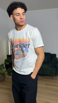 T-shirt blanc avec un imprimé graphique coloré représentant un lecteur de cassette et les textes « Wrangler » et « Keep on Runnin' ». Associé à un pantalon noir.