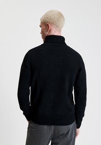 Maglione nero a collo alto in maglia con polsini e orlo a coste, caratterizzato da una finitura testurizzata. Progettato per una vestibilità comoda, vista dalla parte posteriore.