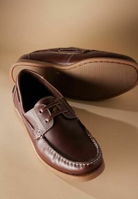 Braune Lederschuhe mit glatter Oberfläche, verziert mit dekorativen Nähten, Schnürsenkeln und einer Gummisohle. Akzentuierungen auf dem Vorderblatt.