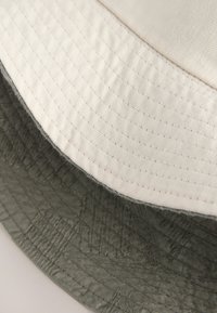 Primo piano dei bordi sovrapposti di un tessuto trapuntato bianco e uno verde scuro, che mostra dettagli di cucitura e texture.