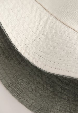 Nahaufnahme der sich  überlappenden Kanten eines weißen und eines dunkelgrünen, gesteppte Stoffes, mit detaillierter Nahtführung und Textur.