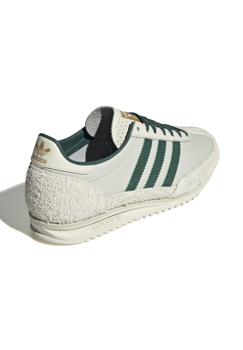 Sneaker en cuir crème avec des rayures vertes, détail en daim texturé à l'arrière et semelle en caoutchouc avec un motif en zigzag. Accents de marque en or.