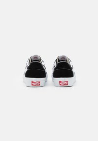 Sorte semsket og hvite lerrets-sneakers med rutete mønster, hvite såler, og rødt logo på hælen, med sømdetaljer.