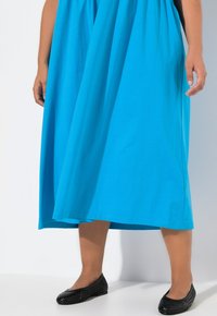 Wibrująca niebieska sukienka do kolan, wykonana z miękkiej bawełny, o luźnym kroju z delikatnymi fałdami. Połączona z czarnymi plecionymi płaskimi butami.