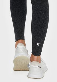Black athletic leggings with a textured finish, paired with white sports shoes featuring a textured sole and adjustable straps.