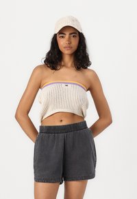 Crop top en tricot crème avec des bords violet et jaune, associé à un short élastique gris foncé. Tissu texturé et coupe décontractée.