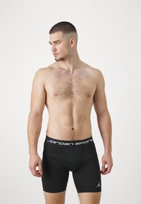 Fekete sportos rövidnadrág, amely szoros illeszkedésű, fehér "Jordan Sports" derékpánttal és logóval, sima, rugalmas anyagból készült.