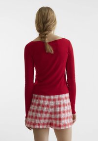 Rotes, geripptes Langarmoberteil mit weitem Ausschnitt, kombiniert mit rot-weißen Karoshorts. Das Outfit zeichnet sich durch eine figurbetonte Silhouette und weichen Stoff aus.