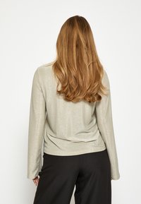 Garums piedurknes tops gaisā metāliskā pelēkā krāsā ar vieglu spīdumu, ar brīvu siluetu un gludu tekstūru, apvienots ar melnām biksēm.