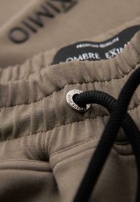 Zbliżenie beżowego elastycznego pasa z czarnym sznurkiem przewleczonym przez metalowy otwór w casualowych spodniach lub szortach.