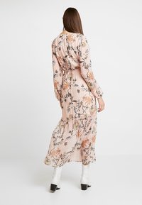 Lange roze bloemenjurk met lange mouwen, geplooid bij de taille en met een gelaagde rokdetaillering. Voorzien van kleurrijke bloemen- en vogelpatronen.