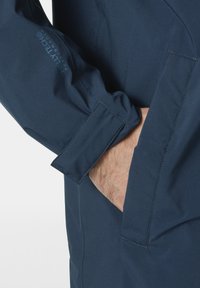 Giacca impermeabile navy con una texture liscia, design dei polsini standard e un logo Helly Tech visibile sulla manica.