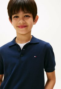 Granatowa koszulka polo o teksturowanym wykończeniu, z krótkim rękawem, z dwiema guzikami na przodzie i małym czerwono-białym logo na piersi.