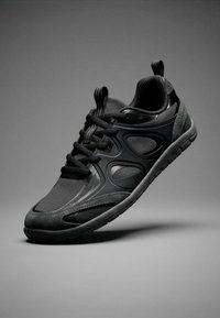 Chaussure de sport noire avec empiècements en mesh et synthétique, design à lacets et semelle texturée, présentée sur fond gris.