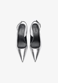 Metalne srebrne slingback pete z ostro konico, ki imajo gladko teksturo in stransko zaponko.
