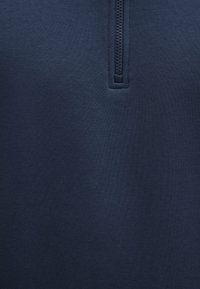 Dunkelblauer Sweatshirt mit strukturiertem Stoff, ausgestattet mit einem Viertel-Reißverschlusskragen und einem glatten, leicht dehnbaren Material.