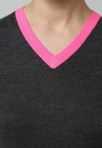 Mörkgrå stickad tröja med V-ringning, med en ljusrosa ribbad halsringning. Mjuk textur, figurnära design.